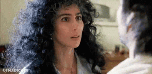 Woman With Curly Hair Looking At Another Woman In Mirror GIF