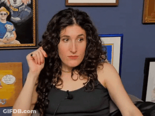 Woman With Curly Hair Sitting In Front Of Blue Wall GIF