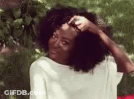 Woman With Curly Hair Sitting In Grass Hand On Head GIF