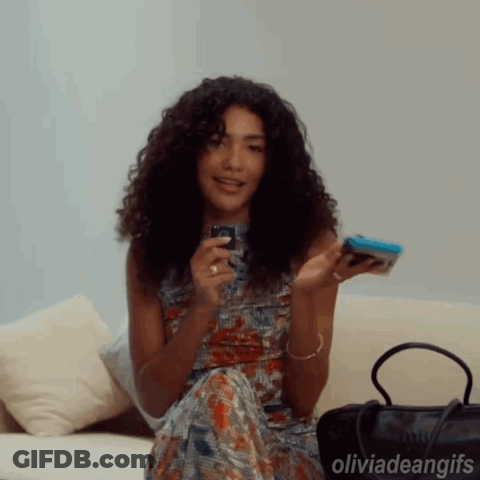 Woman With Curly Hair Sitting On Couch Holding Cell Phone GIF