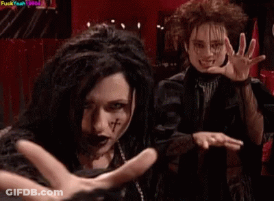 Woman With Dreadlocks And Cross On Face Next To Man In Black Jacket GIF