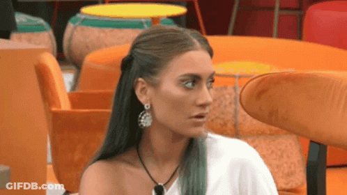 Woman With Earrings And Necklace Sitting In Room With Orange Chairs GIF