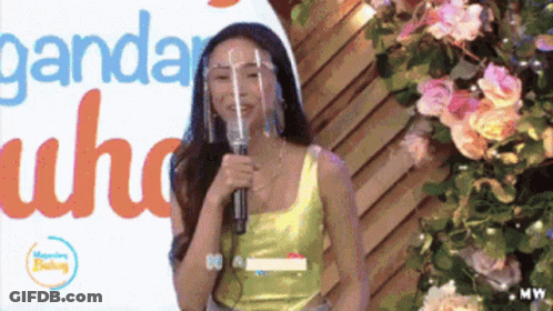 Woman With Face Shield Speaking Into Microphone In Front Of Ganda Sign GIF