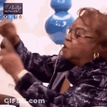 Woman With Glasses And Blue Jacket Sitting On Couch Holding Remote GIF