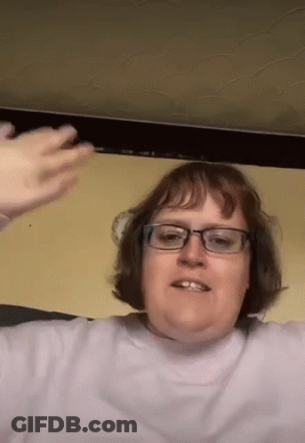 Woman With Glasses In Purple Shirt Sitting In Front Of Yellow Wall GIF