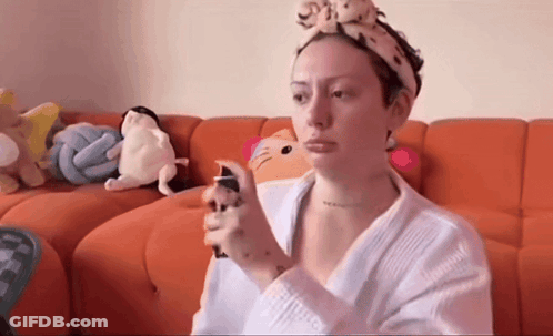 Woman With Headband Spraying Face On Orange Couch GIF