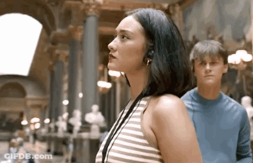 Woman With Headphones Next To Man In Blue Shirt In Museum GIF