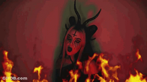 Woman With Horns And Cross Face In Front Of Fire GIF