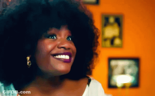 Woman With Large Afro Smiling In Front Of Picture Wall GIF