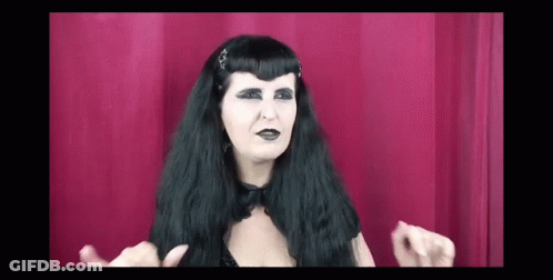 Woman With Long Black Hair And Black Makeup Making Funny Face In Front Of Red Curtain GIF