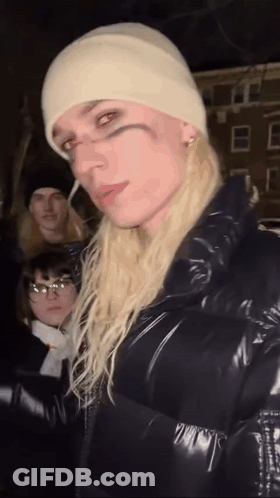 Woman With Long Blonde Hair In White Beanie And Black Jacket GIF