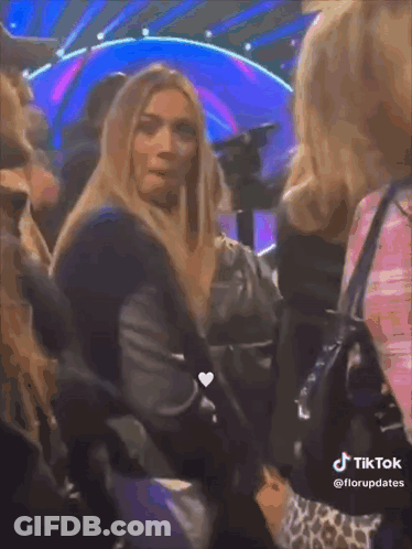 Woman With Long Blonde Hair Sitting In Crowd TikTok Watermark GIF