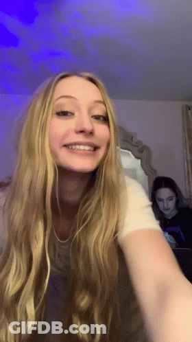 Woman With Long Blonde Hair Smiling In Mirror While Another Woman Looks On GIF