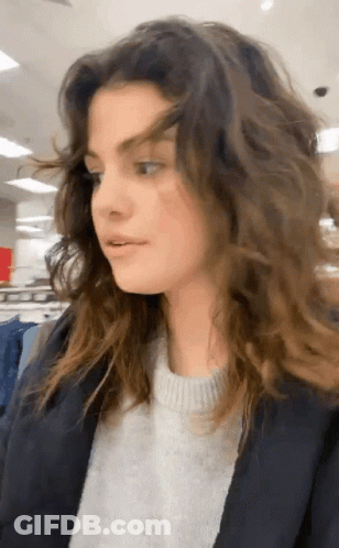 Woman With Long Curly Hair In Sweater And Jacket In Store GIF