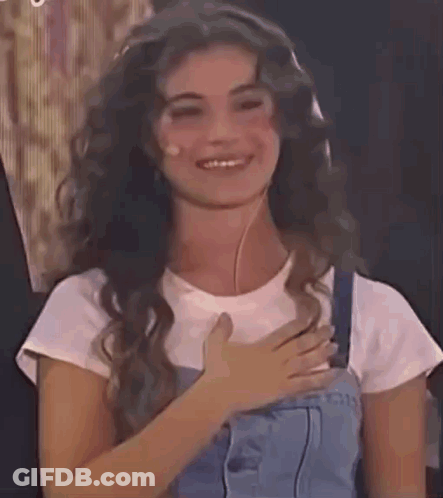 Woman With Long Curly Hair Smiling Hand On Chest GIF