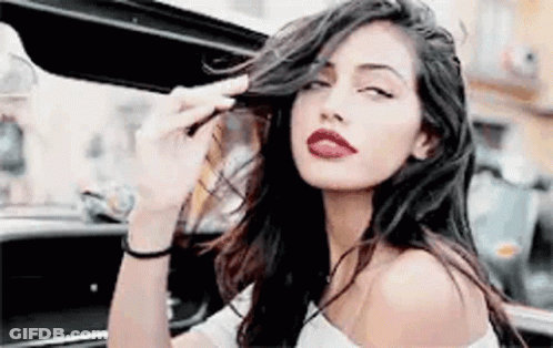Woman With Long Hair And Red Lips Sitting In Car With Open Door GIF