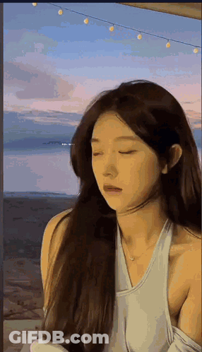 Woman With Long Hair Standing In Front Of Water Eyes Closed White Tank Top GIF