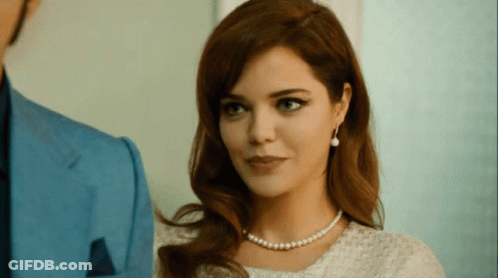 Woman With Pearl Necklace And Earrings Looks At Man In Blue Suit GIF