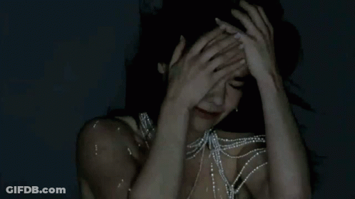 Woman With Pearl Necklace Holding Head In Pain GIF