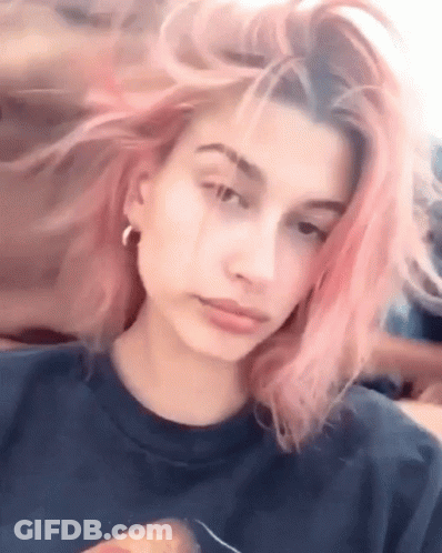 Woman With Pink Hair In Blue Shirt And Earrings Looking At Camera GIF