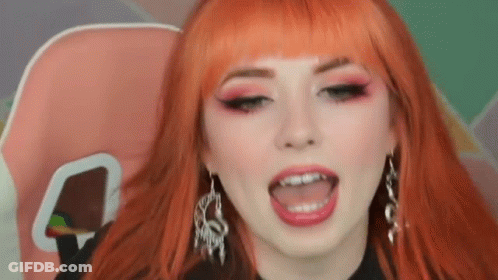 Woman With Red Hair And Earrings Sitting With Tongue Out GIF