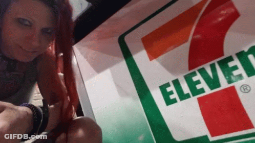 Woman With Red Hair Next To 7-Eleven Sign GIF