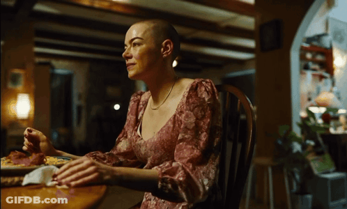 Woman With Shaved Head Sits At Table With Food GIF