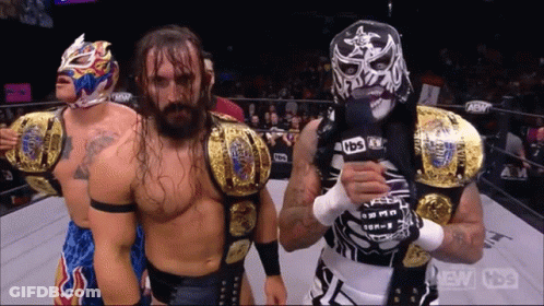 Wrestler In Mask Holding Microphone With Two Wrestlers GIF