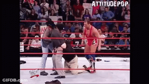 Wrestler Kneeling In Ring With Referee Behind GIF