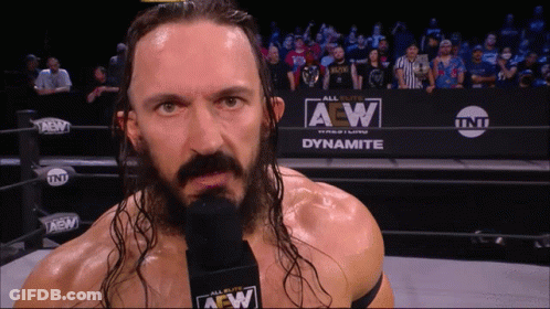 Wrestler With Long Hair And Microphone In Front Of Dynamite Sign GIF