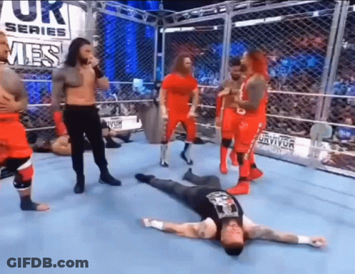Wrestlers Standing Around Man Laying On Floor GIF