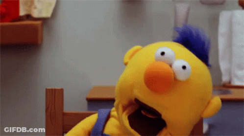 Yellow Sesame Street Puppet With Blue Mohawk Sitting GIF