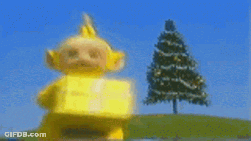 Yellow Teletubbies Carrying Box In Front Of Christmas Tree GIF