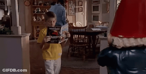 Young Boy Holding Book Next To Santa Claus Statue GIF