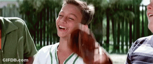 Young Boy In Baseball Uniform Laughing Holding Bat GIF