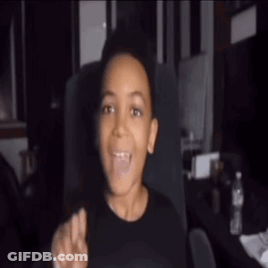 Young Boy In Black Shirt Sitting With Tongue Out GIF