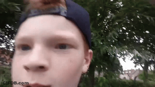 Young Boy In Blue Hat Standing In Front Of Trees GIF