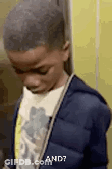 Young Boy In Blue Jacket Looking Down Against Yellow Wall GIF