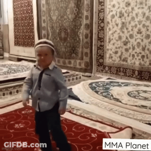 Young Boy In Blue Shirt And Tie Standing On Rug GIF