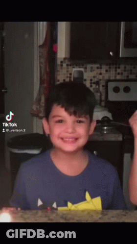 Young Boy In Blue Shirt Smiling In Front Of Microwave And Stove GIF