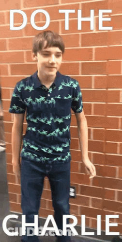 Young Boy In Front Of Brick Wall With Words Do The Charlie GIF