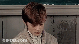 Young Boy In Sweater Sitting In Front Of Chalkboard GIF