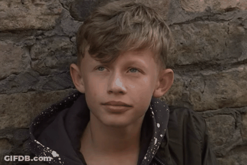 Young Boy Leaning Against Stone Wall Looking At Camera GIF
