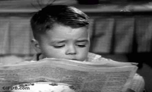 Young Boy Reading Newspaper At Table GIF