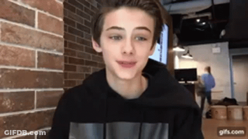 Young Boy Smiling In Front Of Brick Wall GIF