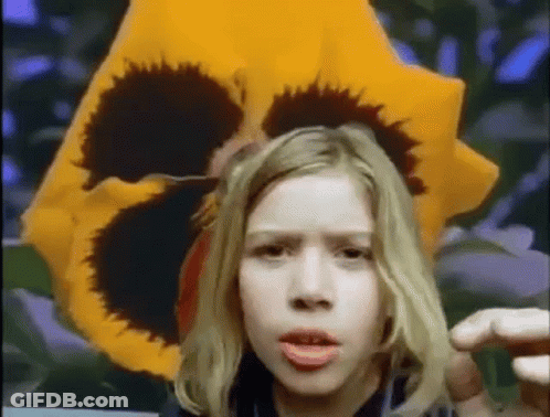 Young Girl Before Yellow Flower With Black Center GIF