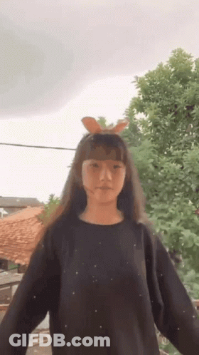 Young Girl In Black Sweater With Bunny Ears Standing In Front Of Tree GIF