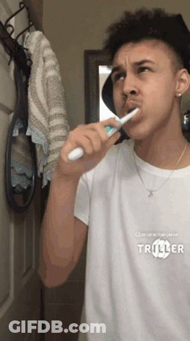 Young Man Brushing Teeth In Mirror Wearing Triller Shirt GIF