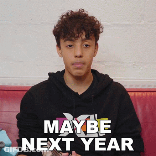 Young Man Curly Hair Sitting In Front Of Maybe Next Year Sign GIF