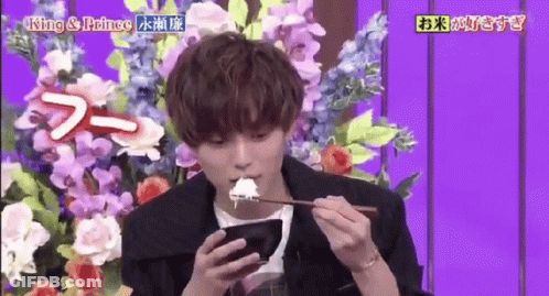 Young Man Eating Rice And Using Phone Beside Flowers GIF